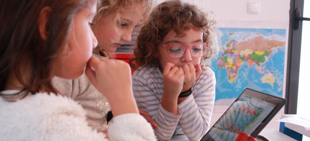 3 kids learning together on laptop with world map in the background
